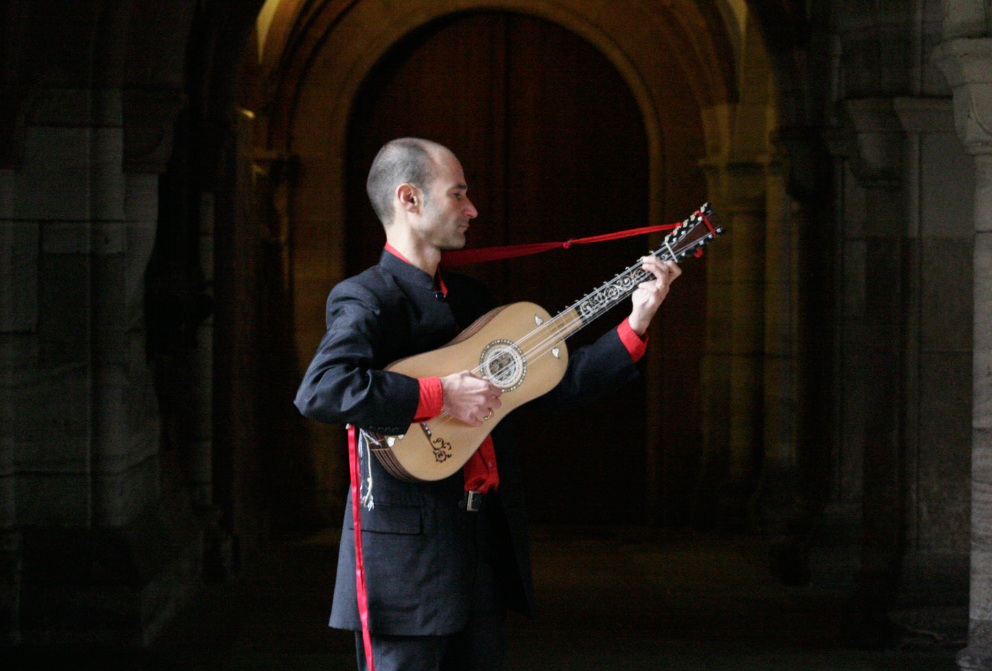 Rosario Conte playing a baroque guitar in front of a dark hallway in a castle.