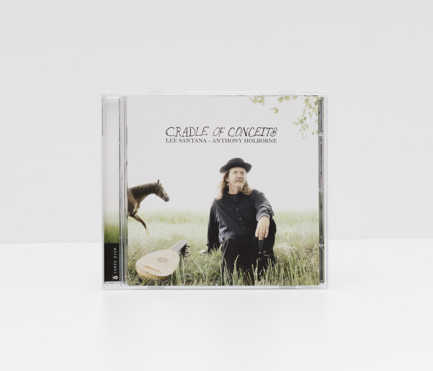 Jewelcase album cover of "Cradle of Conceits" by Lee Santana, showing the artist sitting in the grass with a lute and a horse. 