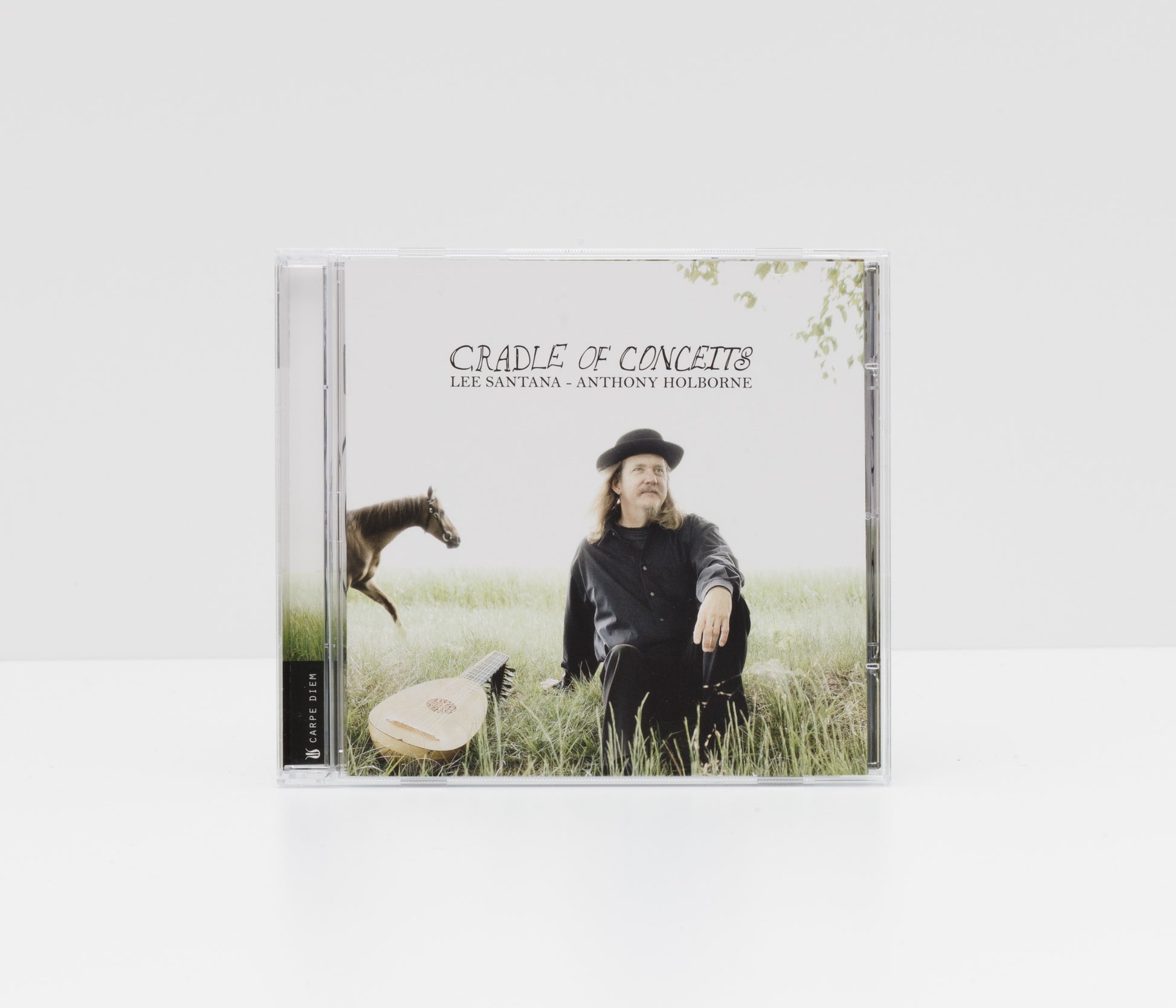Jewelcase album cover of "Cradle of Conceits" by Lee Santana, showing the artist sitting in the grass with a lute and a horse. 