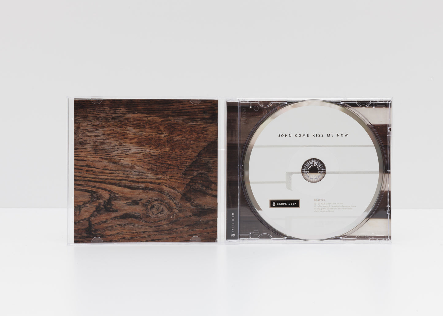 Jewelcase detail of the album "John come kiss me now" by La Beata Olanda showing a wooden structure and the CD. 