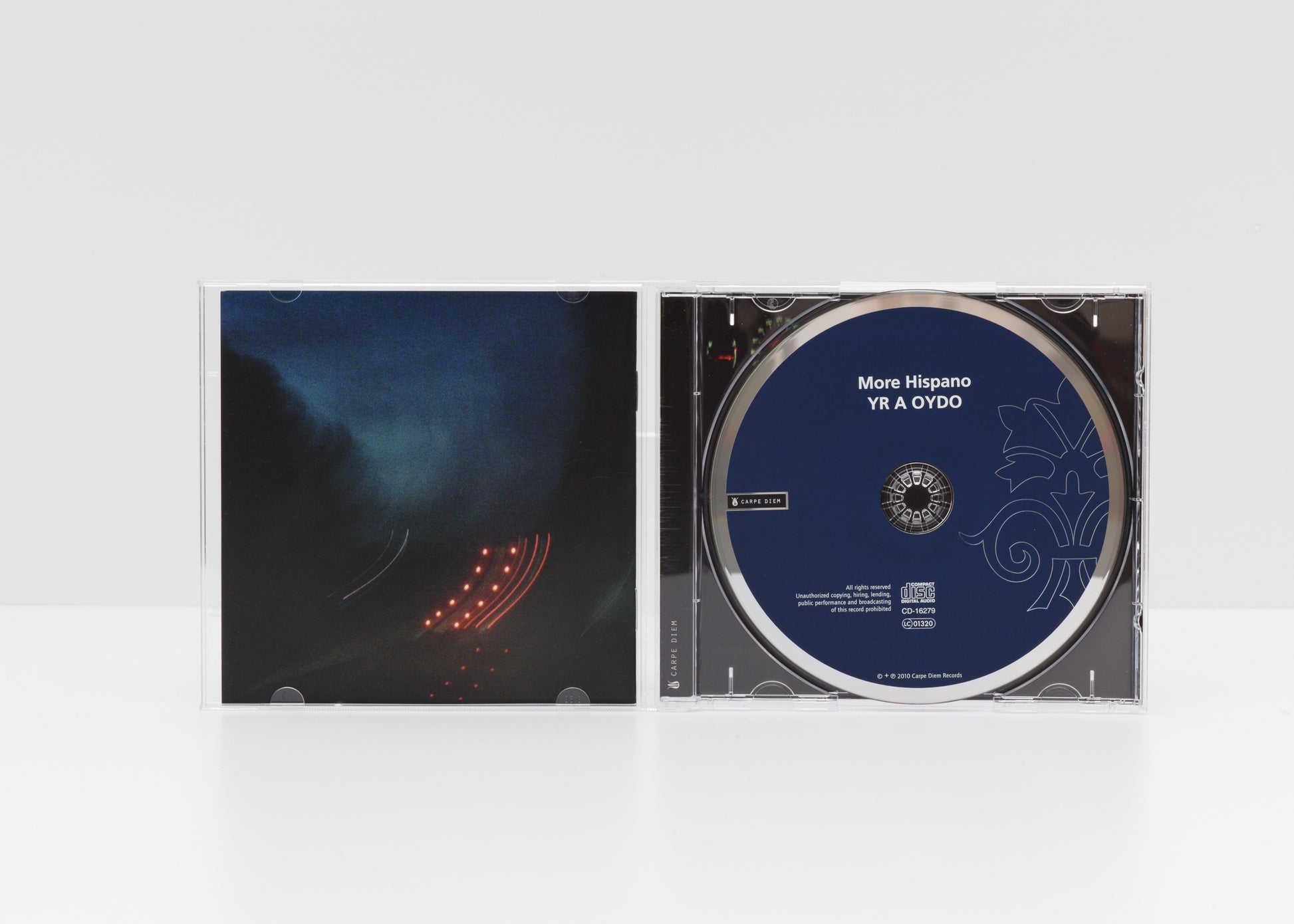 Jewelcase detail of the album "Yr a oydo" by More Hispano (Vicente Parrilla) & Raquel Andueza, showing gloomy car lights in the dark, and the CD. 